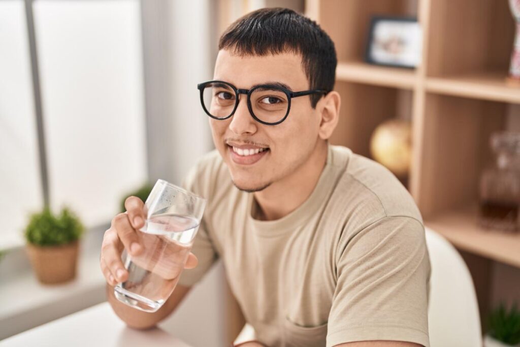 a man raises a glass of clear liquid that may be alcohol to his lips